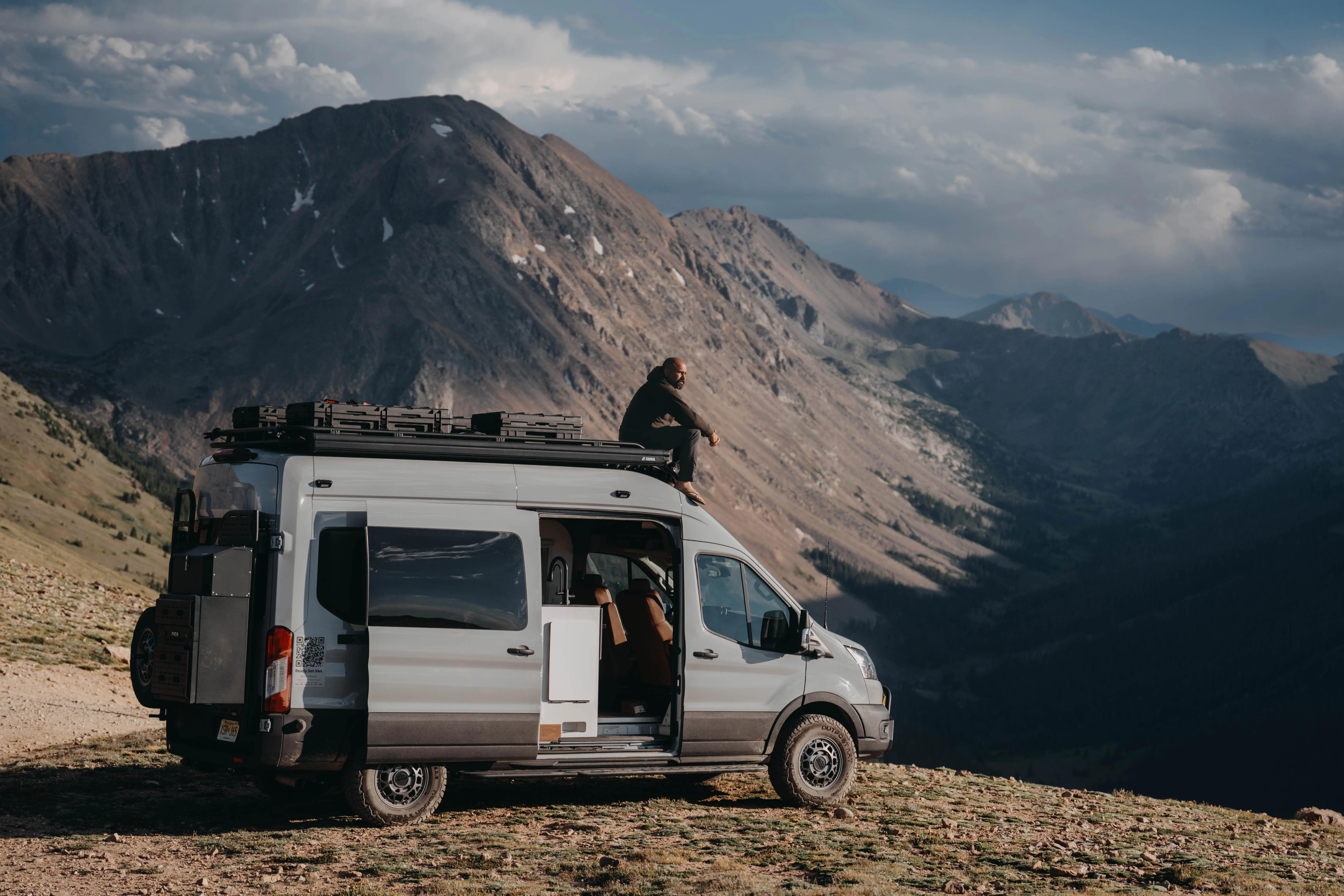 The 148 Highline parked on a ridgeline at Jones Pass, Colorado, door open, roof rack loaded, at golden hour.